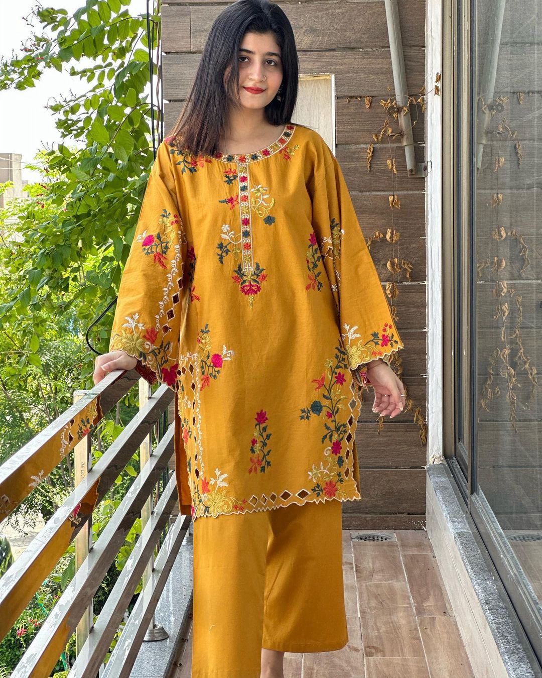 Woman wearing a mustard yellow embroidered outfit standing on a balcony.
