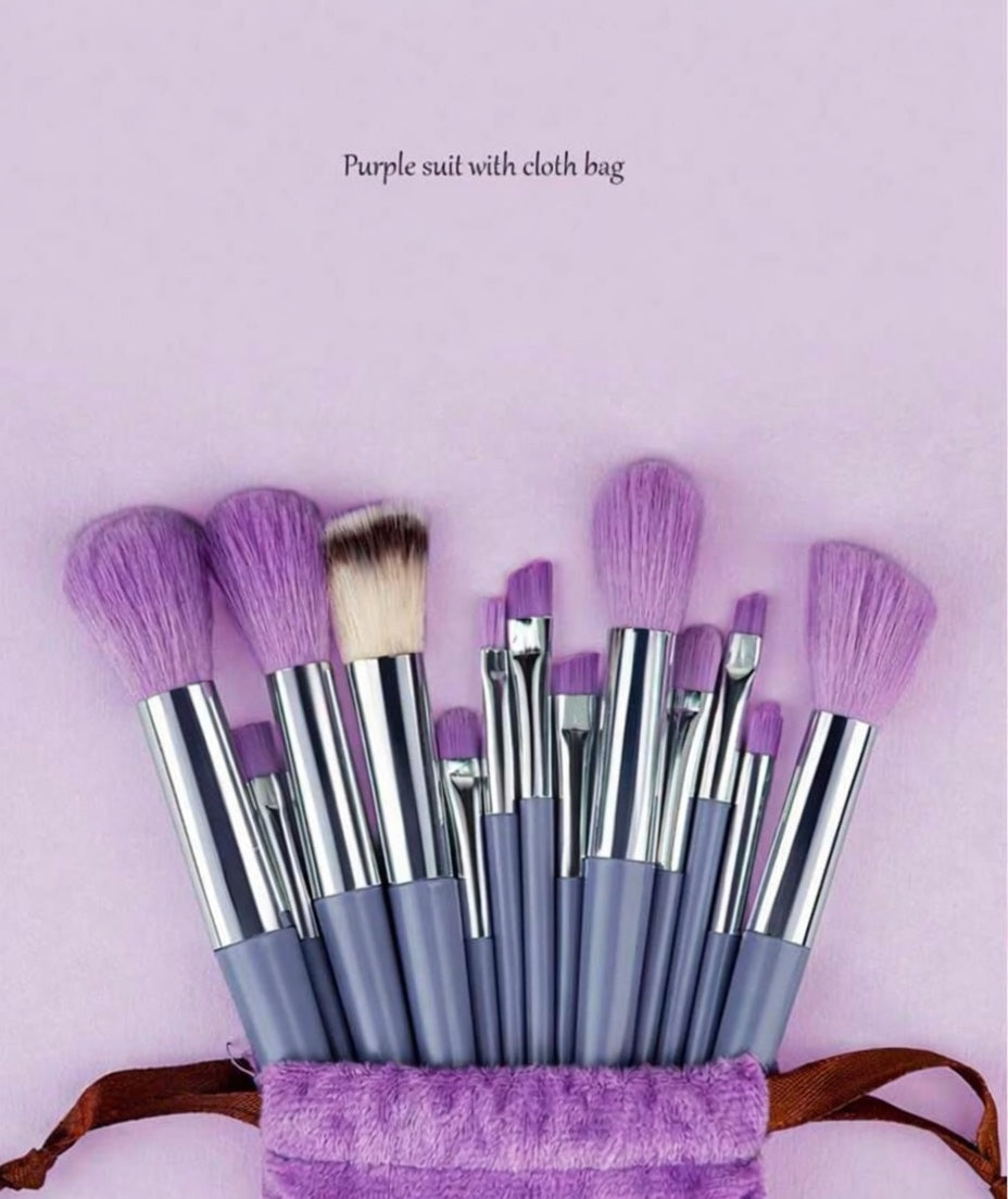 Set of makeup brushes with purple bristles in a purple bag on a light pink background