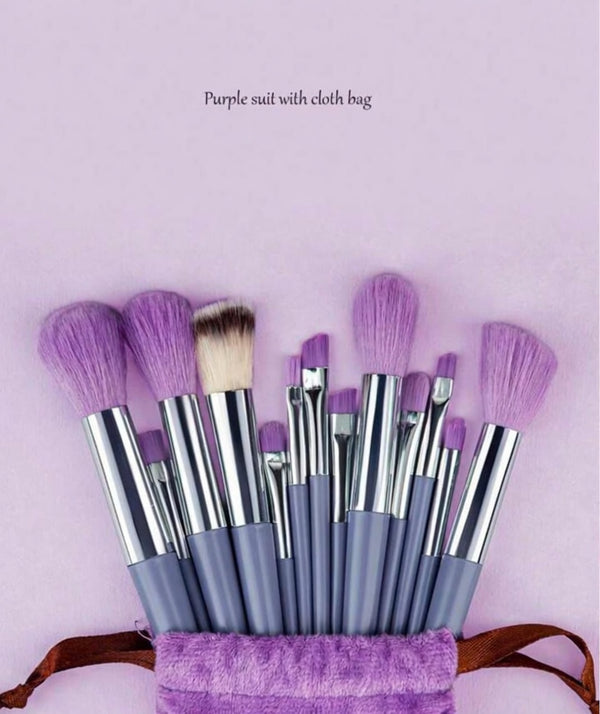 Set of makeup brushes with purple bristles in a purple bag on a light pink background