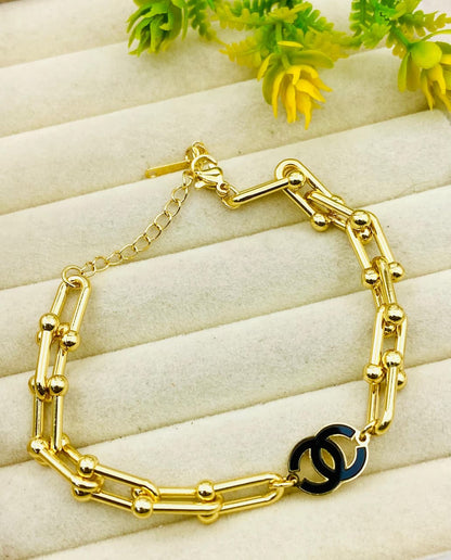 Gold bracelet with a black clasp on a light wooden surface with green leaves.