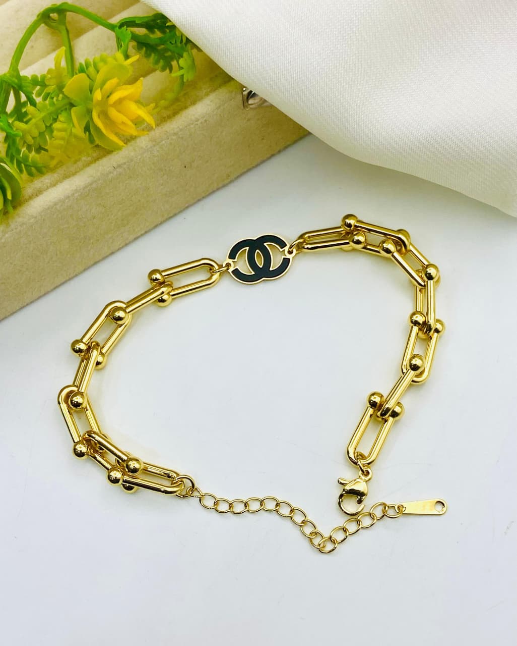Gold chain bracelet with a black and gold clasp on a white surface.