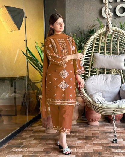 Woman in a brown embroidered outfit standing next to a wicker chair with cushions.