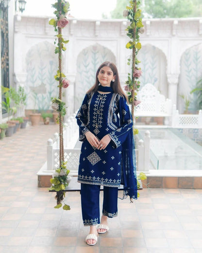 Woman in a blue embroidered outfit standing in a decorated outdoor setting.