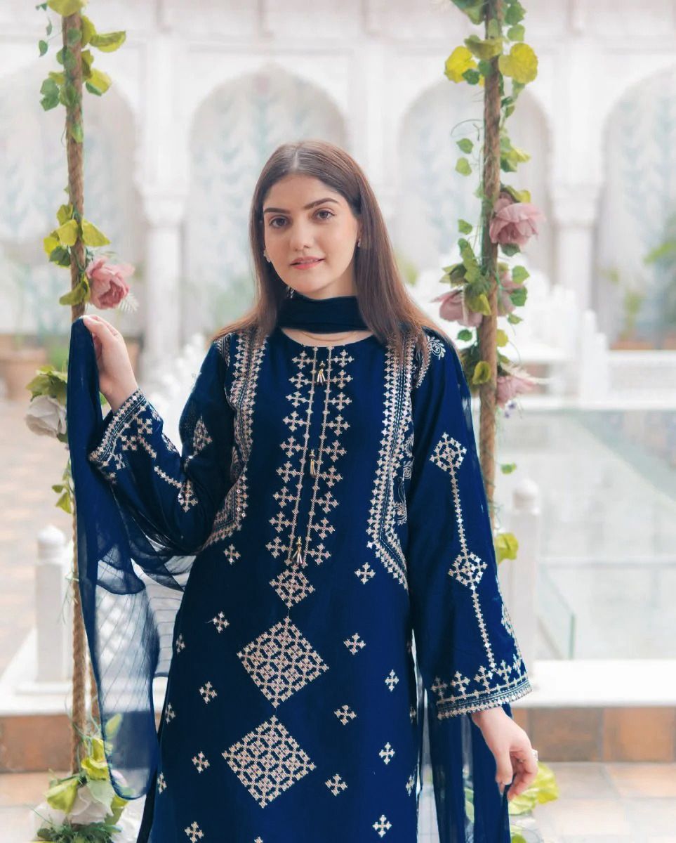 Woman wearing a blue embroidered traditional outfit in a decorative setting with plants.