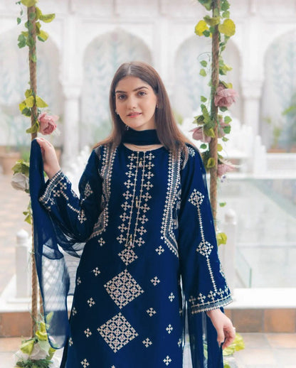Woman wearing a blue embroidered traditional outfit in a decorative setting with plants.