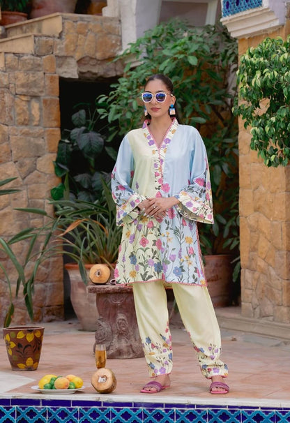 Woman in a floral outfit standing outdoors with plants and a stone wall in the background