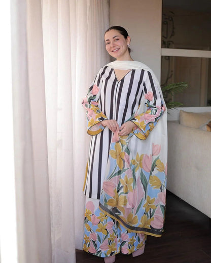 Woman wearing a floral and striped dress in a room with curtains and a couch.