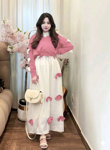 Woman wearing a pink sweater and white dress with pink floral patterns in a room.