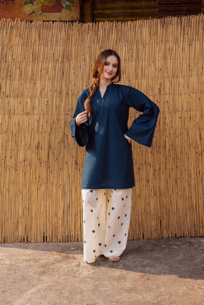 Woman wearing a dark blue top and light-colored pants with heart patterns against a bamboo wall.