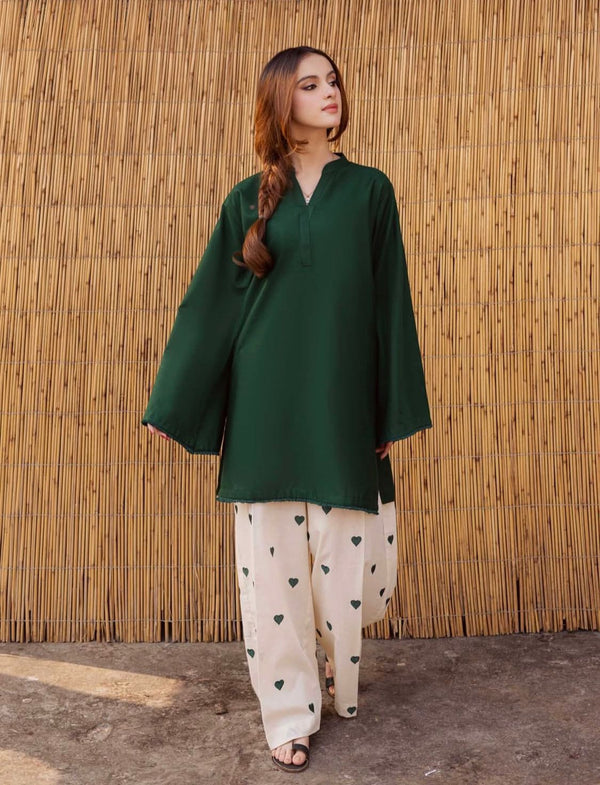 Woman wearing a green top and white pants with black patterns against a wooden background