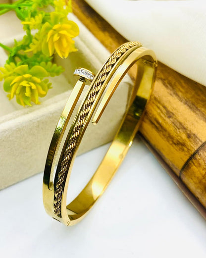 Gold bracelet with intricate design on a white surface with yellow flowers and wooden elements.