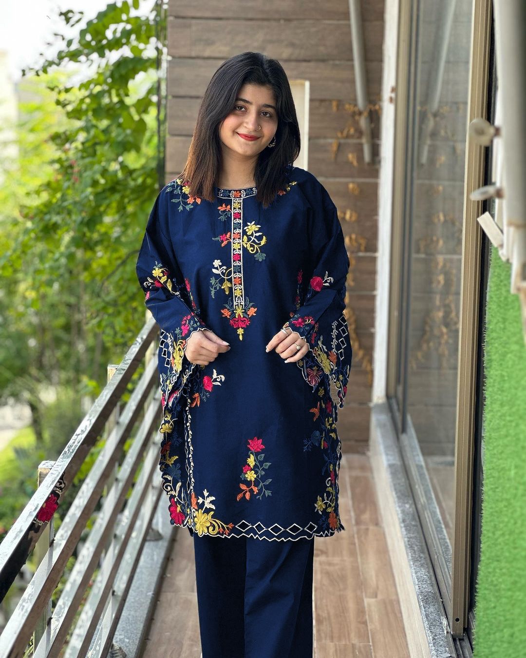 Woman wearing a navy blue embroidered outfit standing on a balcony.