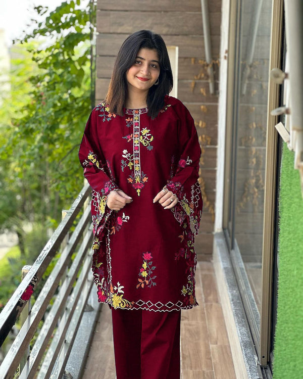 Woman wearing a maroon embroidered outfit standing on a balcony.