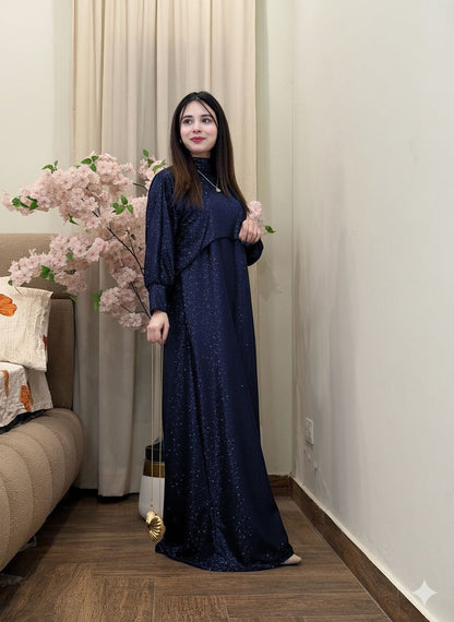 Woman in a navy blue dress standing in a room with a couch and decorative flowers.