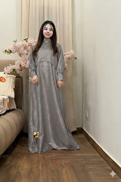 Woman in a long silver dress standing in a room with flowers and a couch.