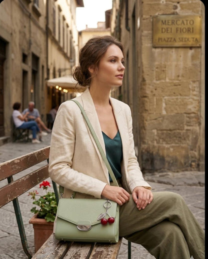 Woman sitting on a bench in an old street with a green handbag.