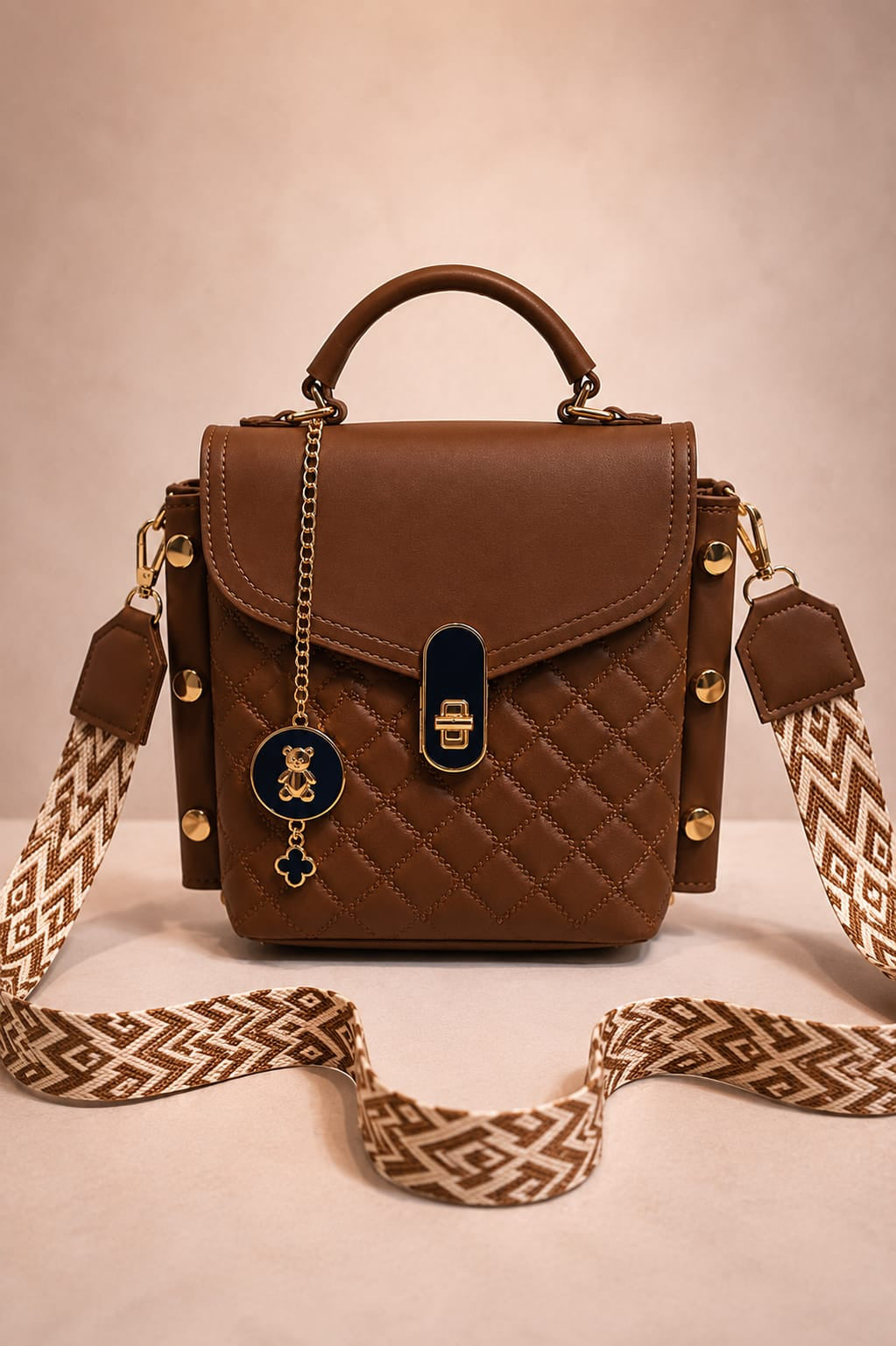 Brown quilted handbag with decorative strap on a beige background