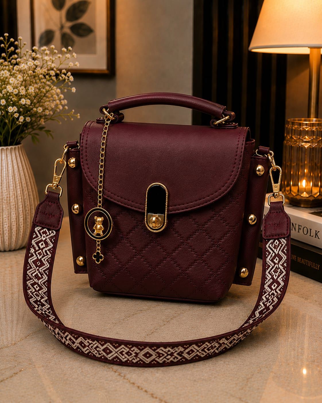 Maroon handbag with gold accents on a surface, with a decorative strap.