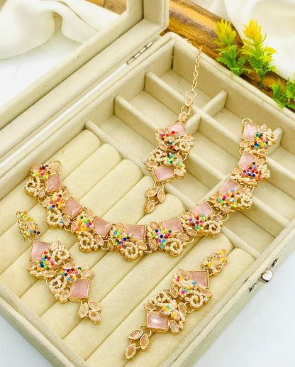Gold necklace with pink stones and colorful accents on a beige jewelry box.