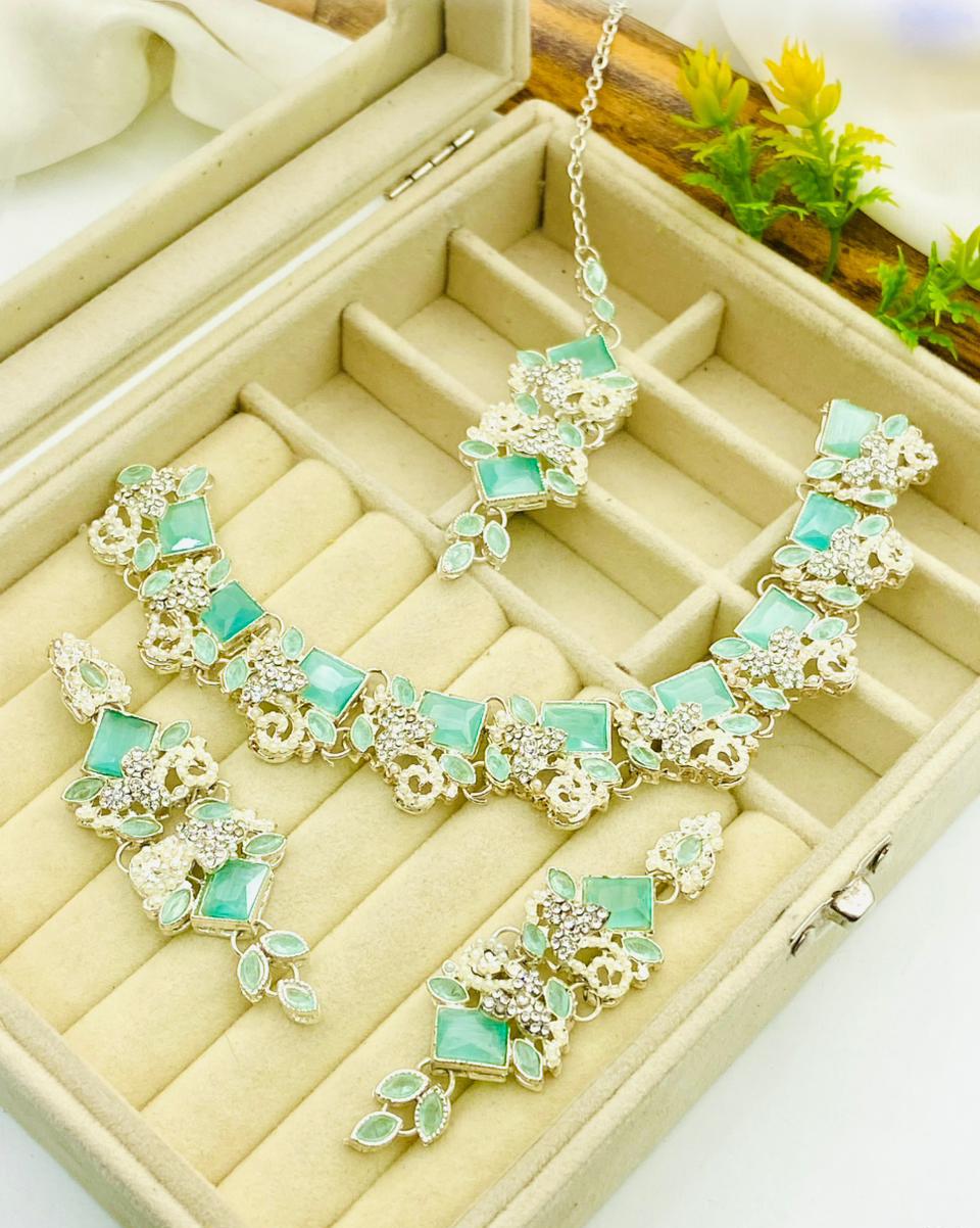 Turquoise and gold necklace on a jewelry box with a plant in the background