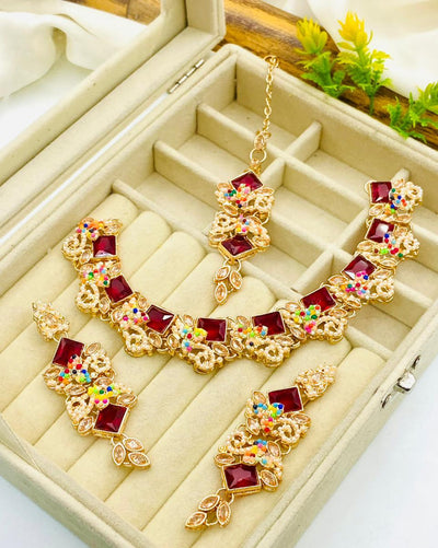 Gold necklace with red gemstones and multicolored stones on a beige jewelry box.