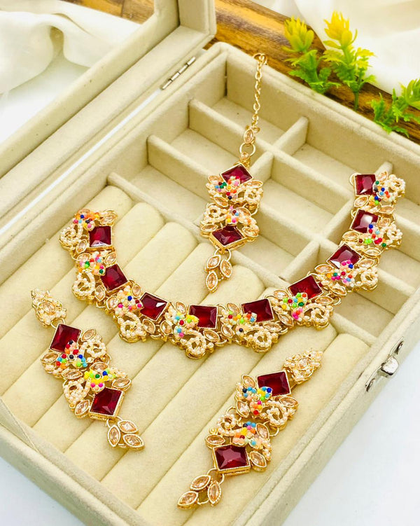 Gold necklace with red gemstones and multicolored stones on a beige jewelry box.