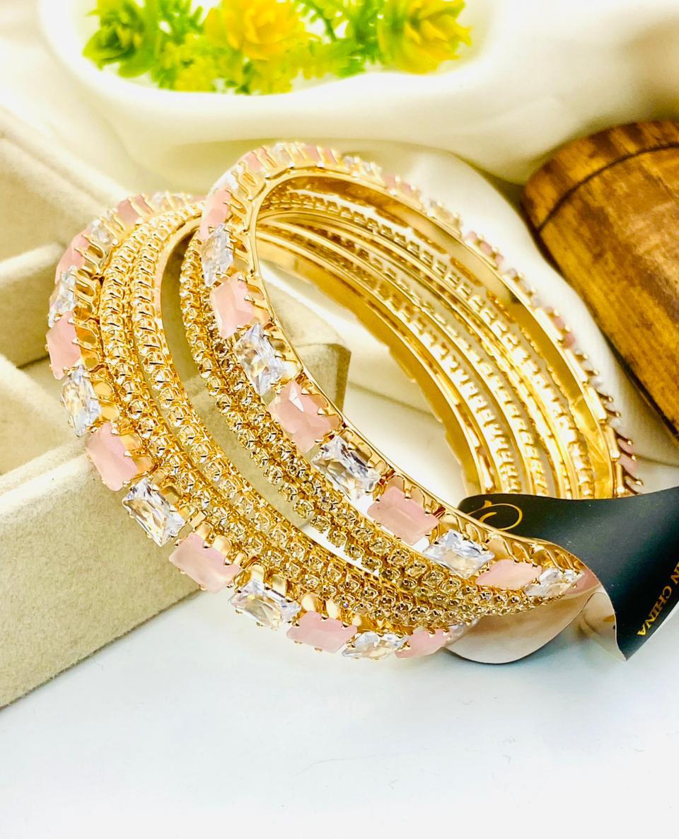 Gold and pink bangles on a white surface with a blurred background