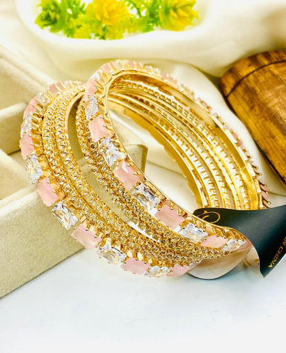 Gold and pink bangles on a white surface with a blurred background