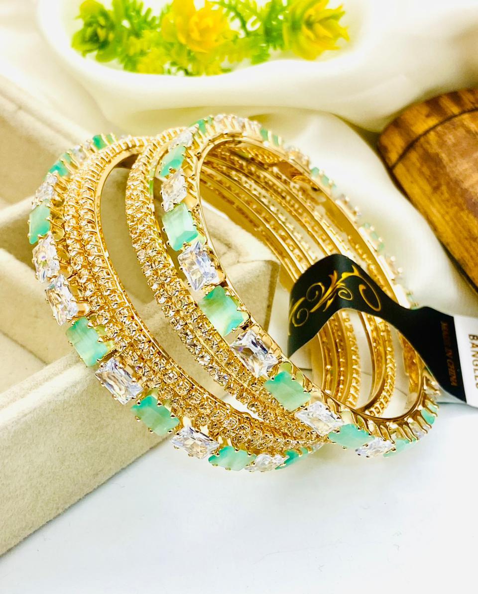 Gold and green beaded bracelets on a white surface with a blurred background