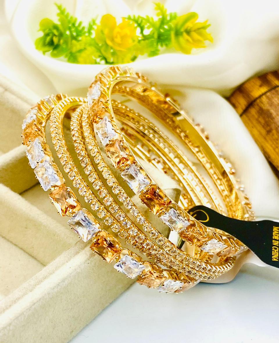 Gold bangles with diamond-like stones on a white surface with a blurred background