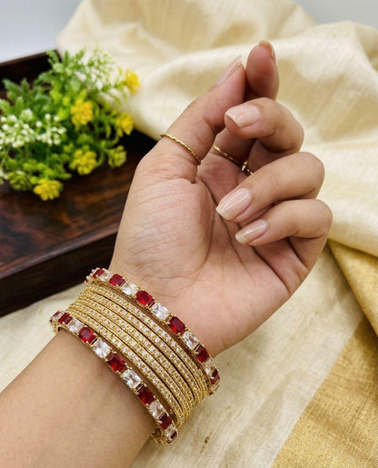 Hand wearing multiple gold and red bangles with a light background