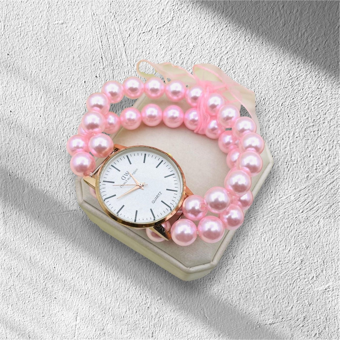 Pink pearl bracelet with a watch on a textured surface