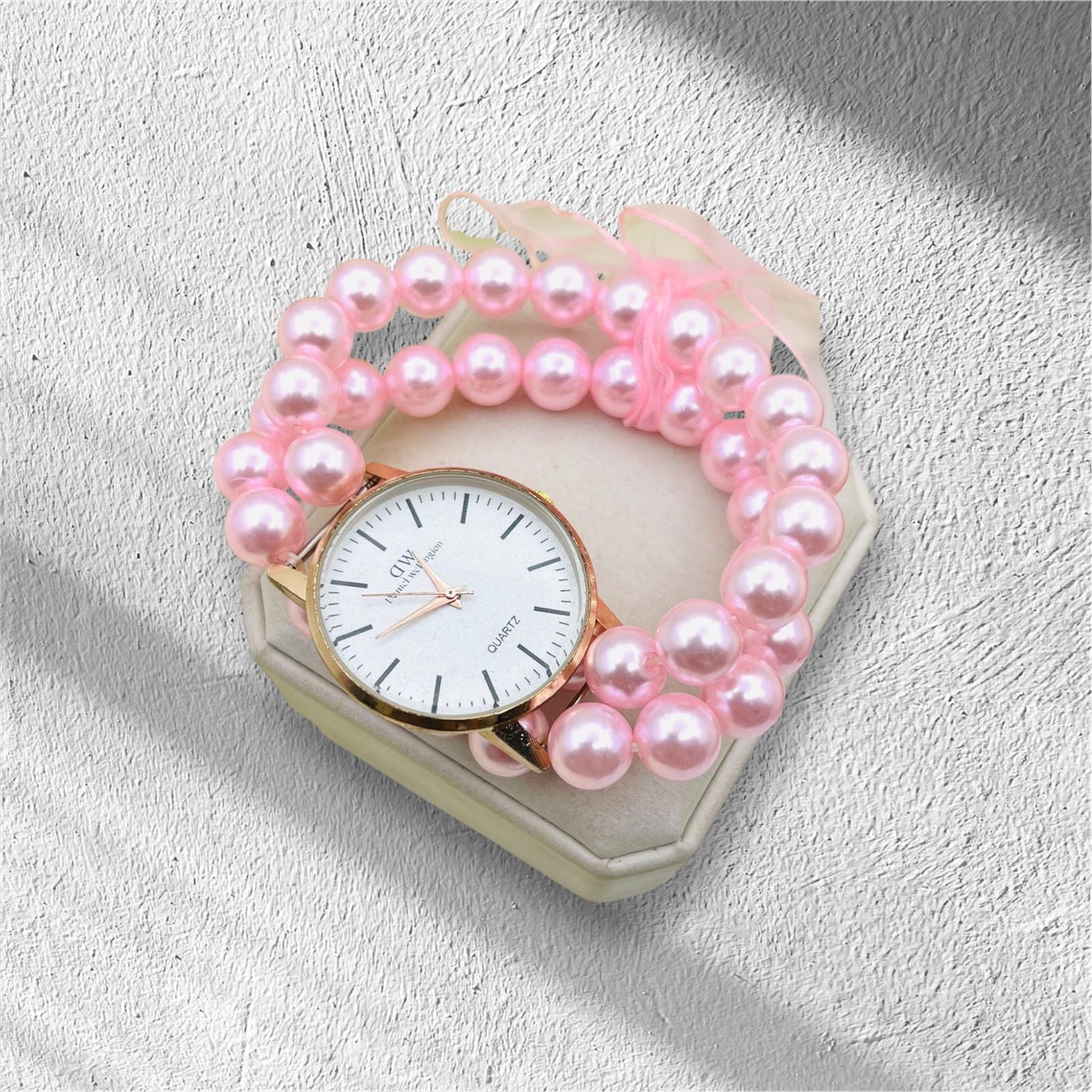 Pink pearl bracelet with a watch on a textured surface