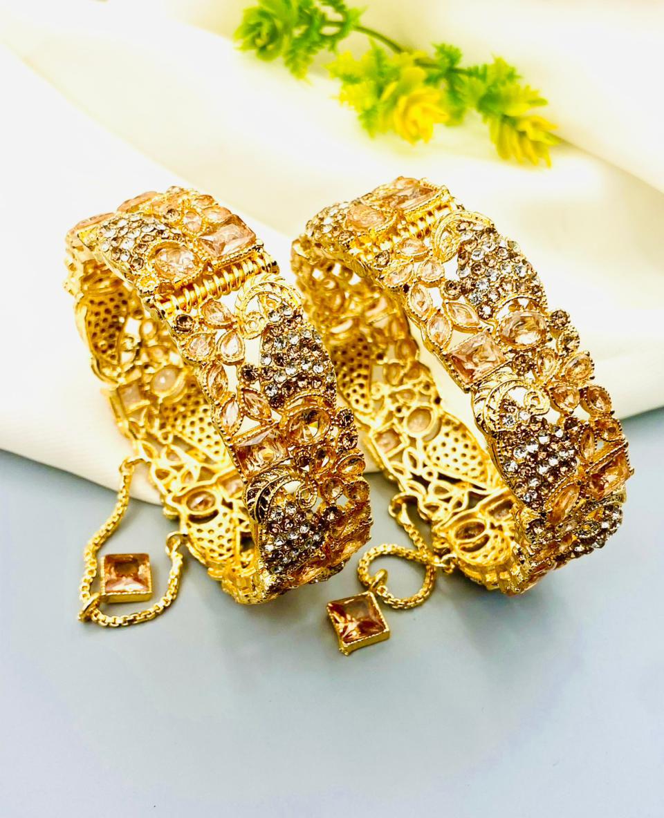 Two gold bracelets with intricate designs on a light background