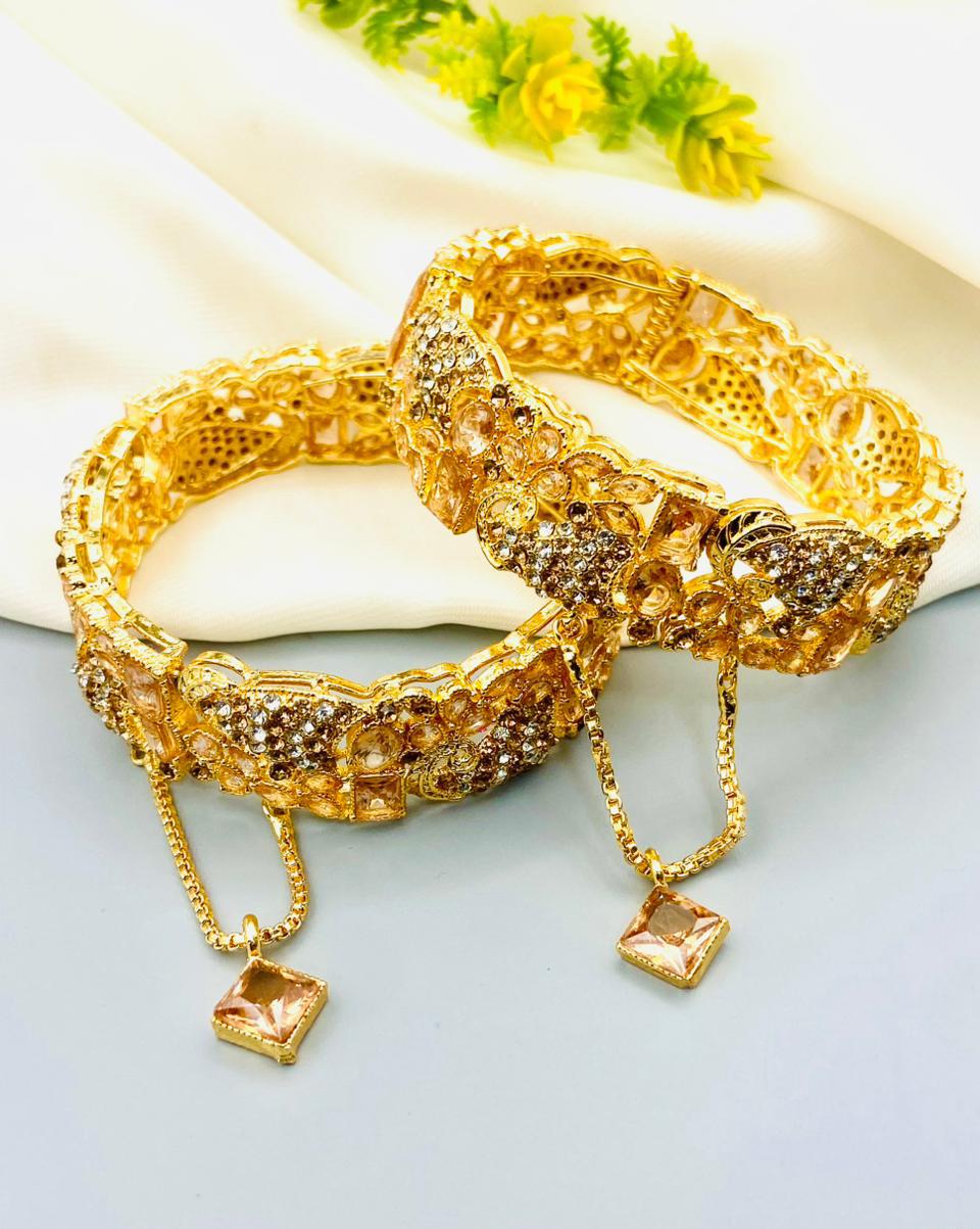 Gold bracelet with intricate design and square charm on a light background
