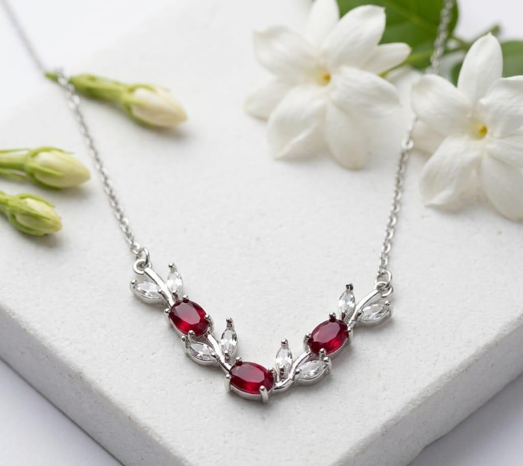 Silver necklace with red gemstones on a white surface with white flowers
