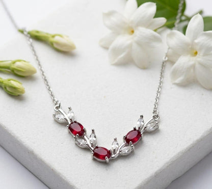 Silver necklace with red gemstones on a white surface with white flowers