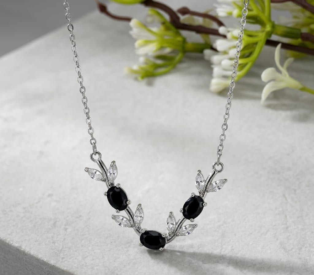 Silver necklace with black stones on a white surface with green flowers in the background