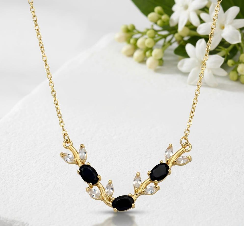 Gold necklace with black and clear stones on a white surface with flowers in the background