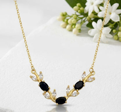 Gold necklace with black and clear stones on a white surface with flowers in the background
