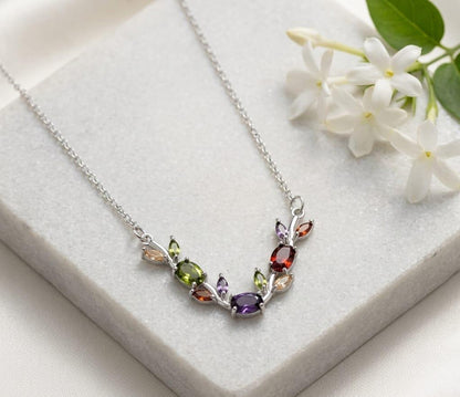 Necklace with multicolored gemstones on a white surface with flowers