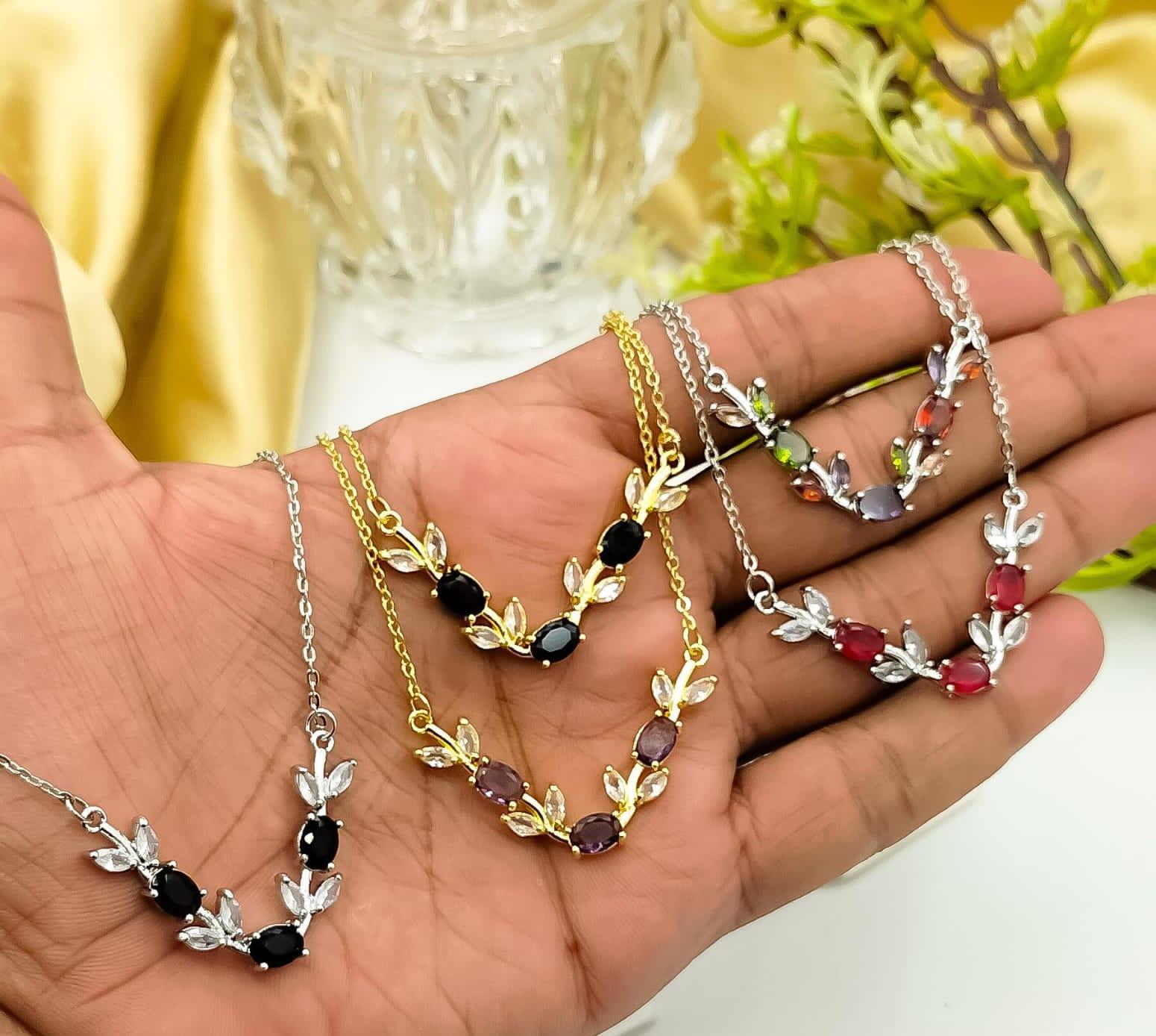 Hand holding four necklaces with different gemstone colors against a blurred background