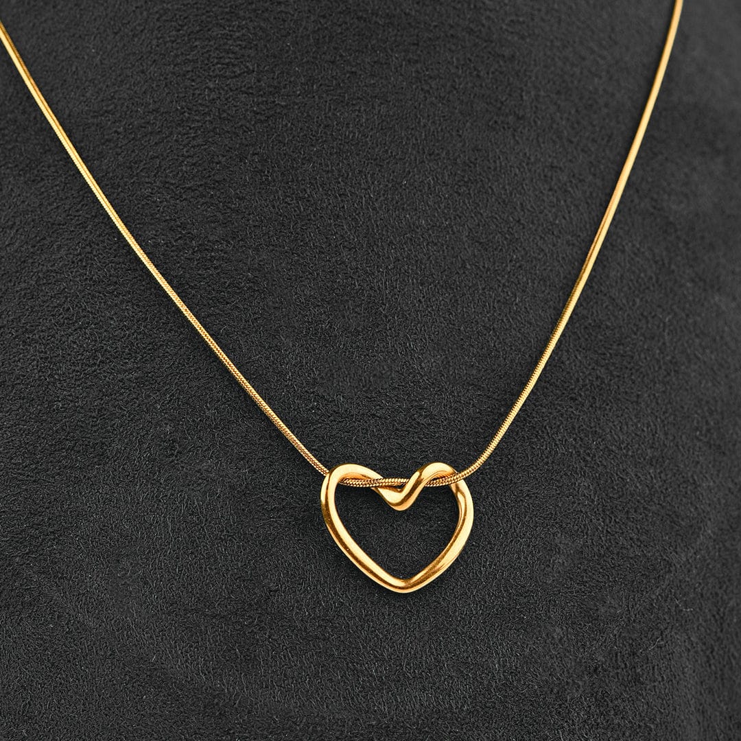 A delicate gold necklace with an open heart pendant featuring a small knot in the center, displayed on a textured black background.