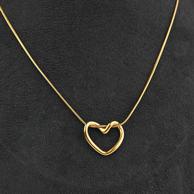 A delicate gold necklace with an open heart pendant featuring a small knot in the center, displayed on a textured black background.
