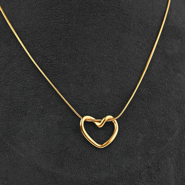 A delicate gold necklace with an open heart pendant featuring a small knot in the center, displayed on a textured black background.