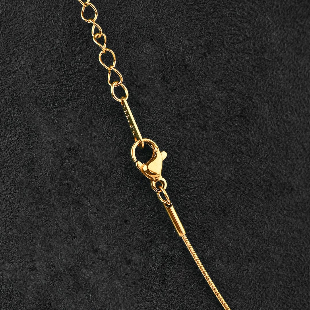 Close-up of a gold-tone chain necklace with a lobster clasp and extender link section, laid diagonally on a textured black background.