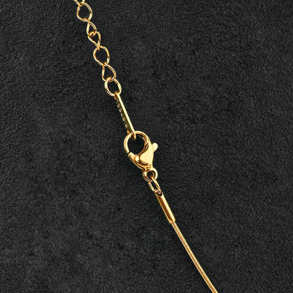 Close-up of a gold-tone chain necklace with a lobster clasp and extender link section, laid diagonally on a textured black background.