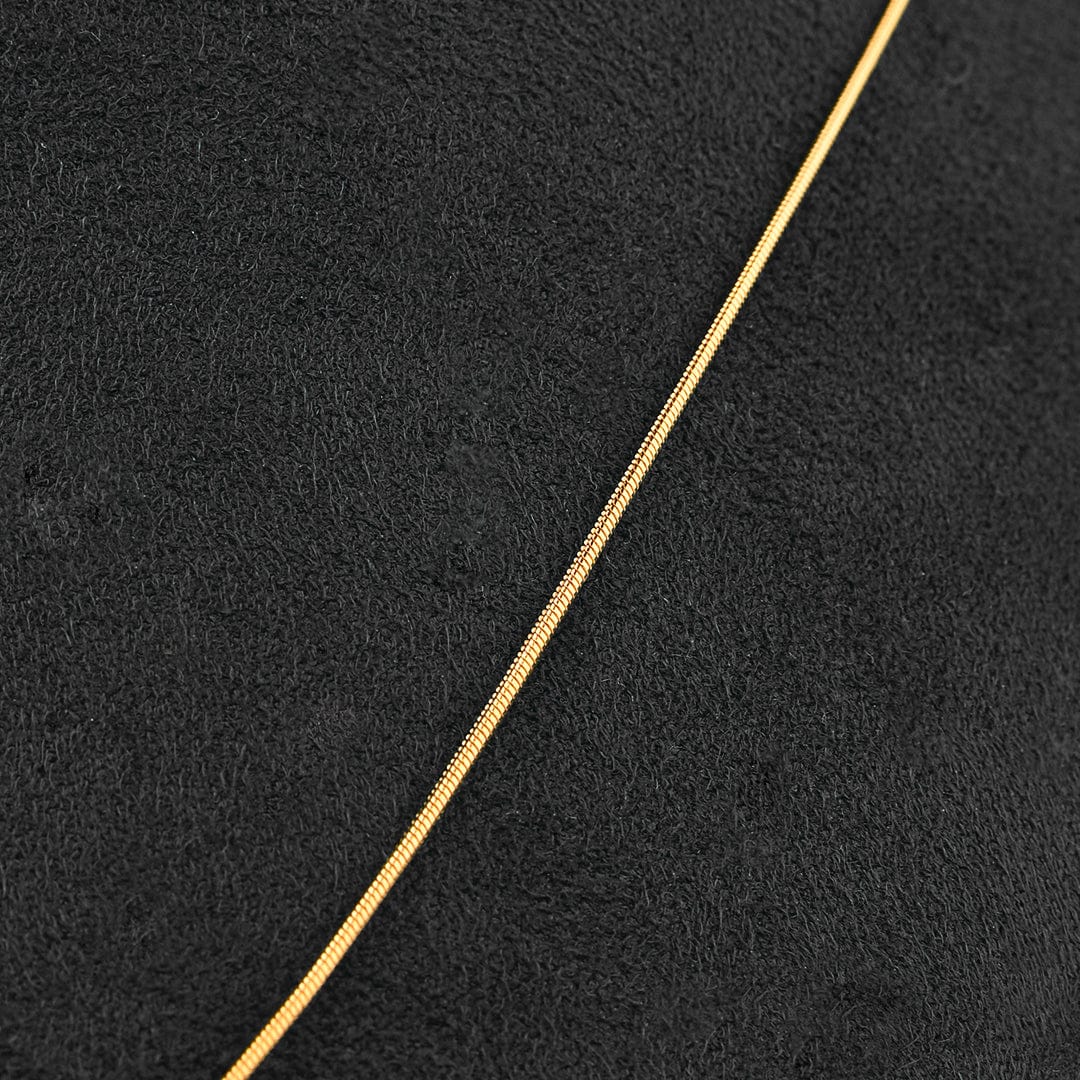 A close-up of a thin gold chain laid diagonally across a textured black surface.