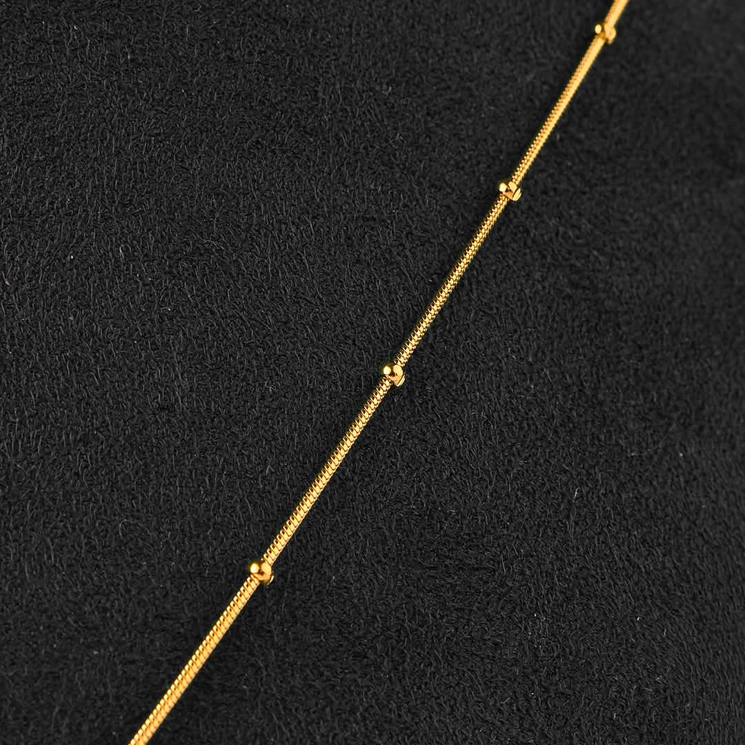A close-up of a delicate gold chain necklace laid diagonally on a textured black background.