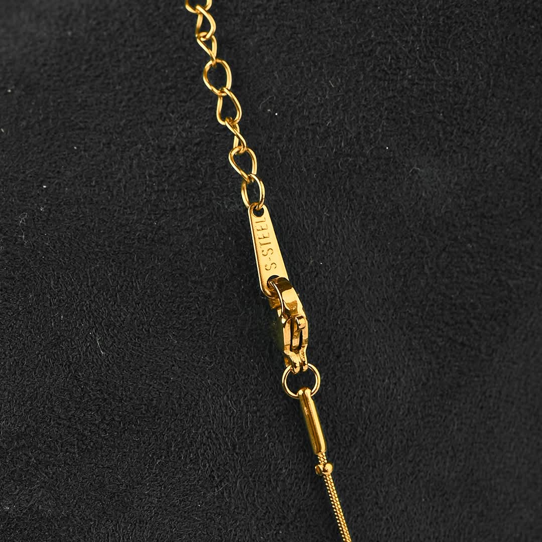 Close-up of a gold-tone chain necklace with a lobster clasp and tag, photographed against a dark textured background. The tag is engraved with 'GUESS'.